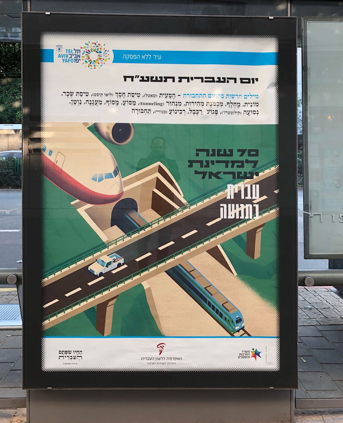 צילום כרזה ליום העברית תשע"ח איור של מטוס, רכבת ורכב על מחלף וכיתוב "עברית בתנועה"